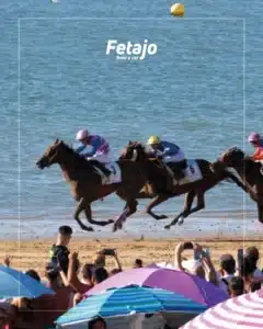 Jockeys racing thoroughbred horses along the beach at the Sanlúcar horse races with spectators watching from the shore
